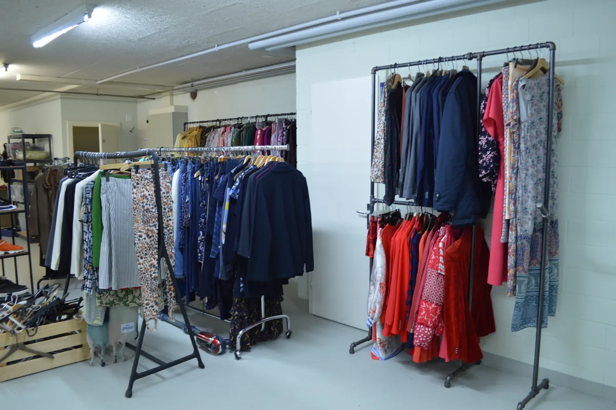 In einem Raum hängen viele Kleider an Stangen.